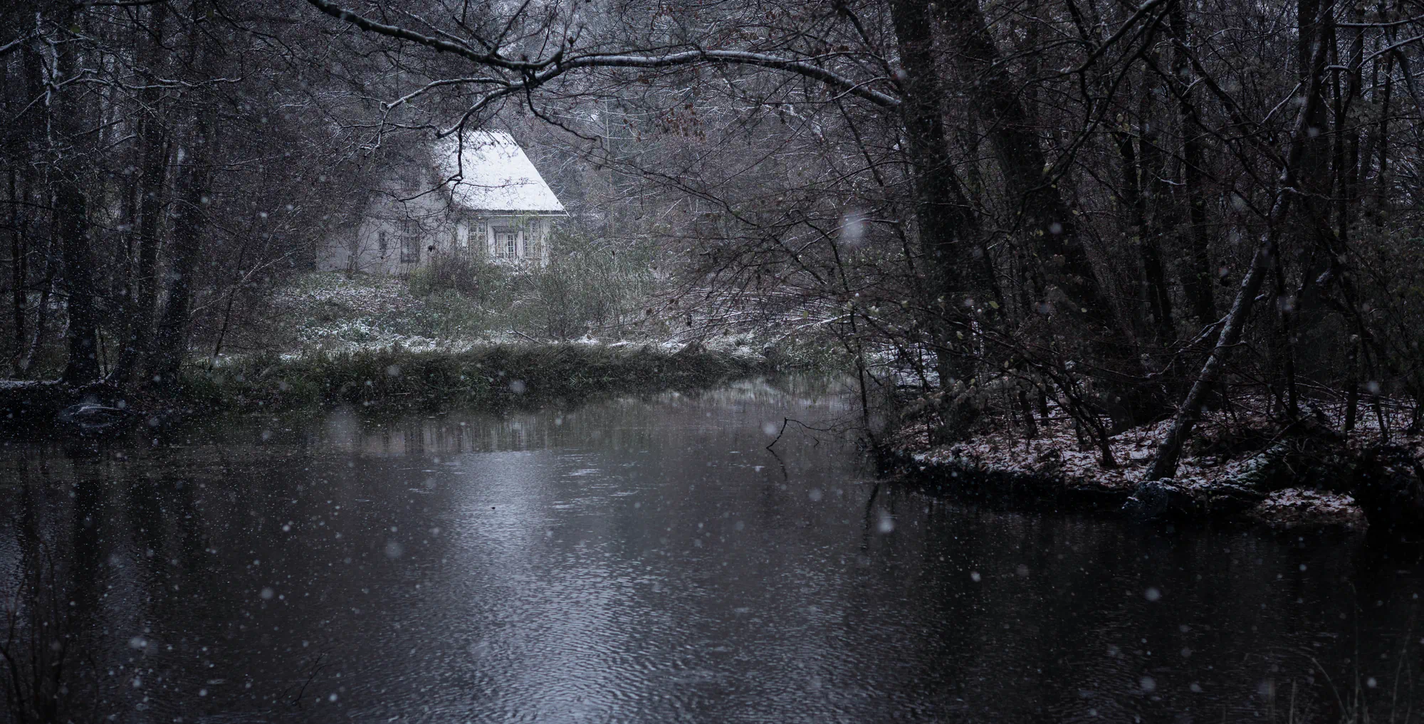house in dark snowy forest near lake